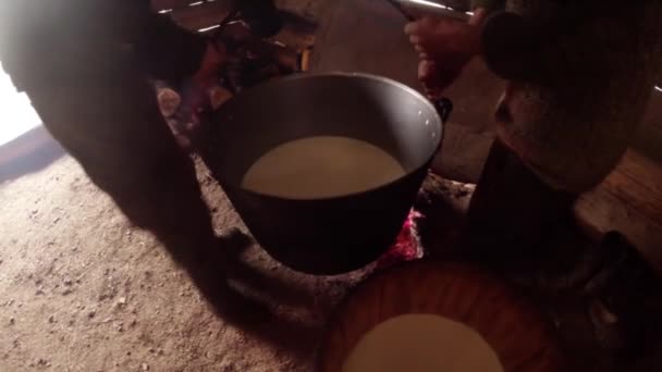 two people pour milk from a heavy metallic boiler in a wooden barrel - Filmati, video