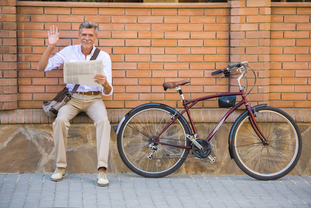Senior man with bicycle is reading a newspaper sitting outdoors. - Foto, immagini