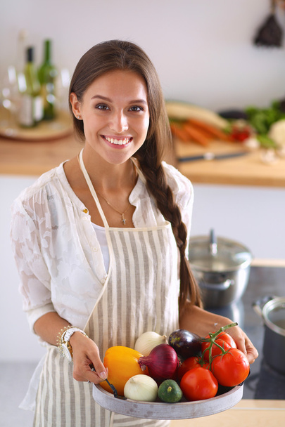Smiling young woman holding vegetables standing in kitchen - Foto, Imagem