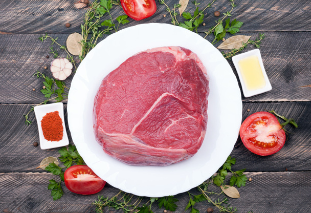 Сырое мясо говядины с травами, специями, оливковым маслом и помидорами на старый
 - Фото, изображение