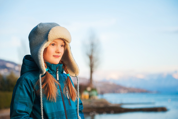 Outdoor portrait of adorable little girl on a nice winter evening, resting by the lake at sunset - Фото, изображение