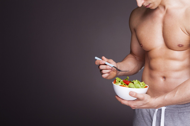 Athletic man holding a bowl of fresh salad - Foto, imagen