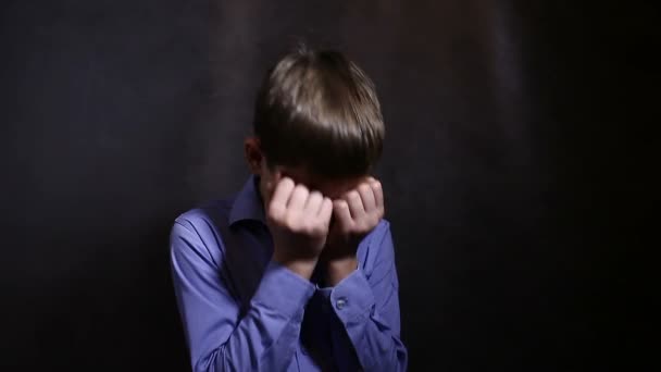 Teenage boy crying upset closed eyes with his hands in a blue shirt, studio background - Footage, Video