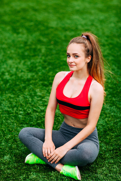 Young fitness girl sitting on green grass . - Foto, Bild