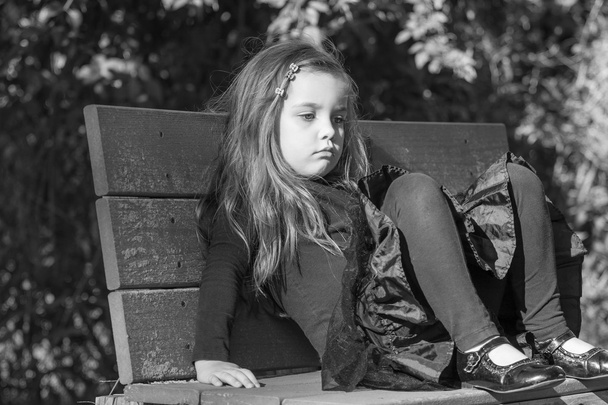 niña cansada o aburrida sentada en un banco, imagen en blanco y negro
 - Foto, imagen