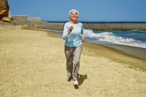 idosa mulher feliz correndo na praia ao longo da costa perto do mar
 - Foto, Imagem