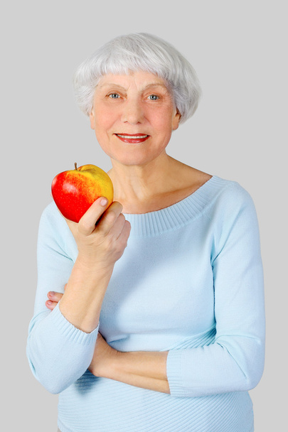mulher idosa com maçã vermelha nas mãos em um fundo leve no estúdio, mãe, avó
 - Foto, Imagem