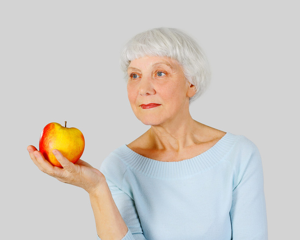 elderly woman with red apple in hands on a light background in the studio, mother, grandmother - Fotografie, Obrázek