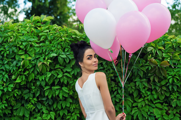 attractive girl with balloons standing next to a hedgerow - Фото, изображение