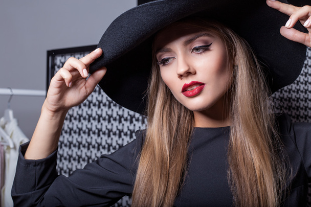 beautiful sexy attractive girl in a black hat with red lipstick in fashion photography in a black dress with a bright evening make-up - Foto, afbeelding