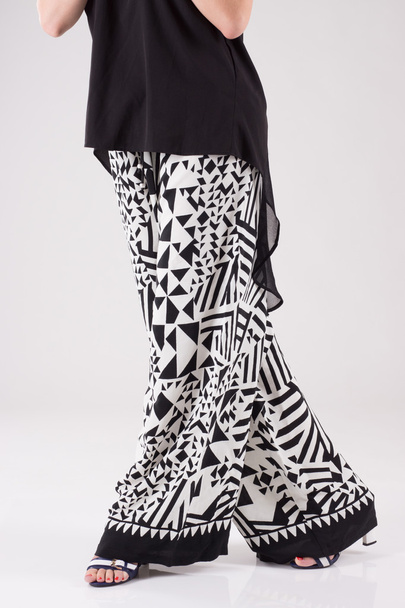 Μπλούζα γυναικεία φορεσιά μαύρο με ένα μακρύ πίσω και ευρύ μαύρο και άσπρο παντελόνι με σχέδιο. - Φωτογραφία, εικόνα