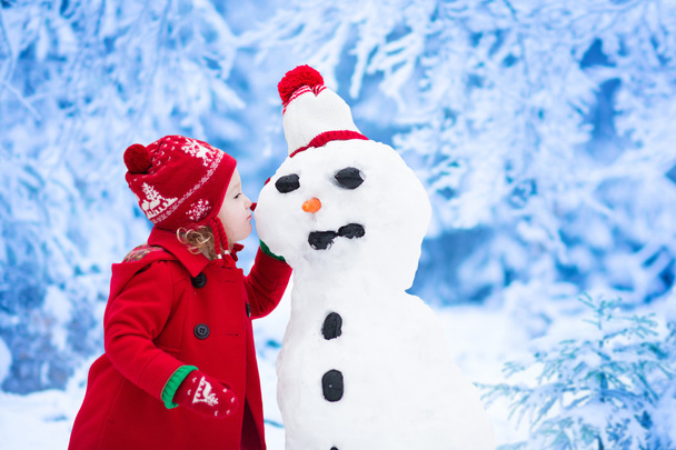 Niña construyendo muñeco de nieve en invierno
 - Foto, Imagen