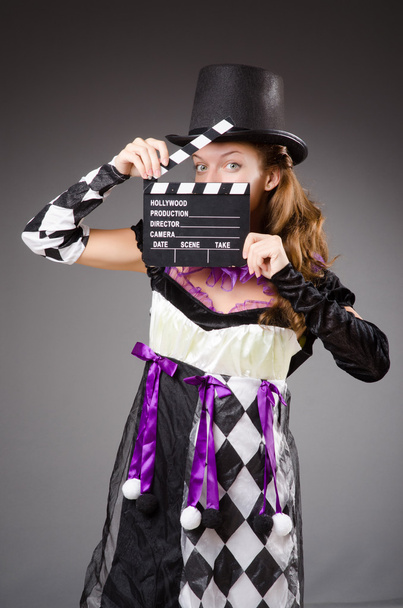 Mooi meisje in jester kostuum Filmklapper houden tegen grijs - Foto, afbeelding