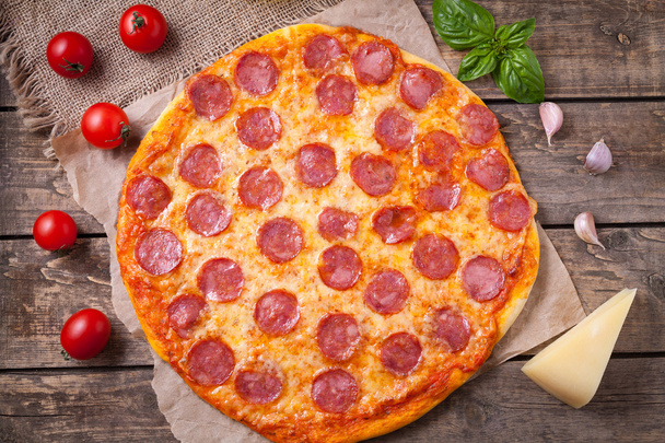 Pizza mediterránea tradicional casera con pepperoni, queso mozzarella, tomates, albahaca y ajo sobre fondo de mesa de madera vintage
 - Foto, imagen