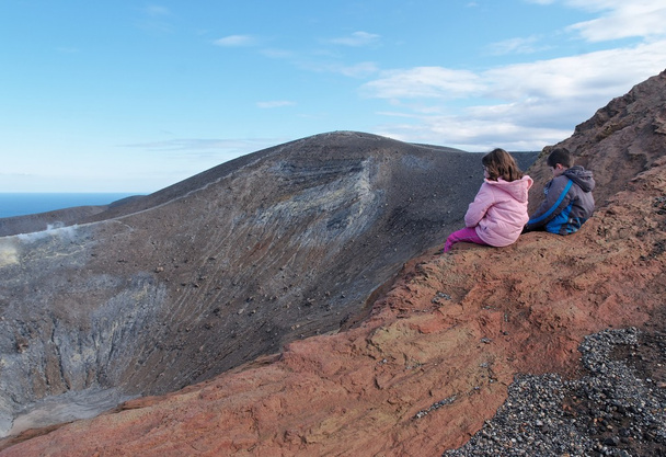 Menina e menino sentados na borda da cratera vulcânica
 - Foto, Imagem