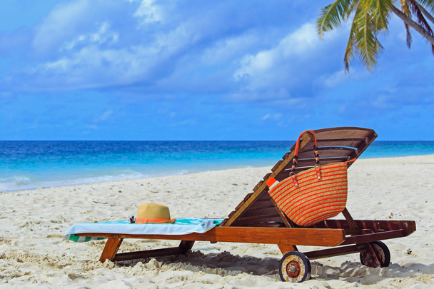 stro hoed en zak op een lounge stoel op tropisch strand - Foto, afbeelding
