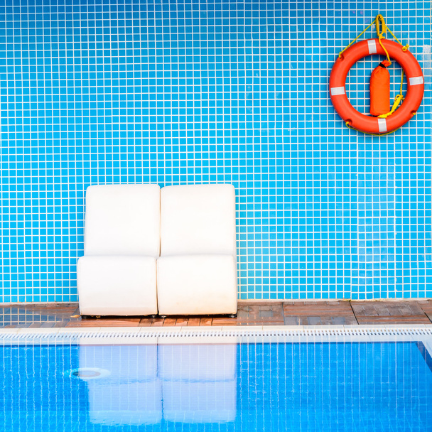Witte stoelen op blauwe achtergrond met een oranje boei van het leven in de buurt van zwembad - Foto, afbeelding
