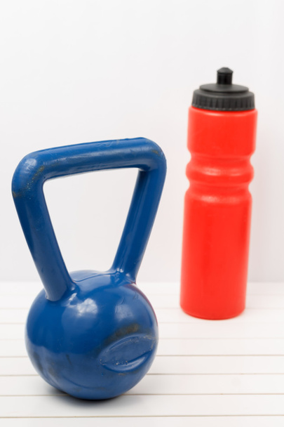 гиревой колокол и бутылка воды на белом деревянном полу
 - Фото, изображение