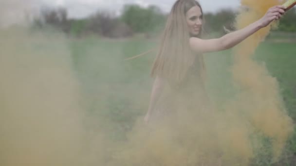 Счастливая молодая женщина в темном платье с цветочным принтом весело проводит время на открытом воздухе в джинсовом поле. Красавица девушка с оранжевой дымовой шашкой кружится и смеется. зеленый фон красочный дым. Рэд
 - Кадры, видео
