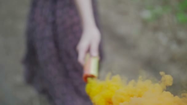 Happy young woman in dark dress with floral print having fun outdoor in orange colorful smoke. Beauty girl holding a colorful orange smoke bomb.wonderful smile. camera follow close up slow motion - Materiał filmowy, wideo
