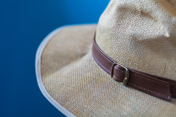 Blurred blue image of a cream hat with white fringe and brown strap - Photo, Image