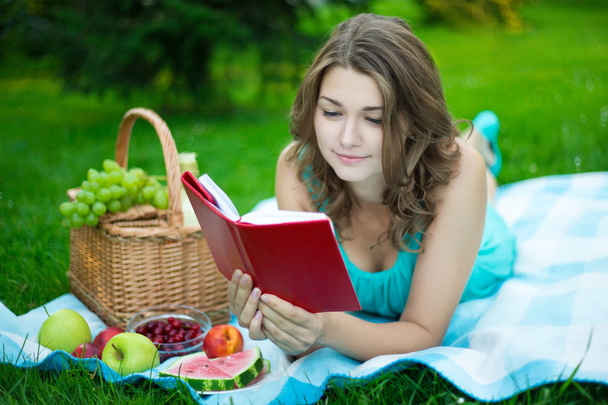 young beautiful woman with picnic basket lying and reading book - Photo, Image