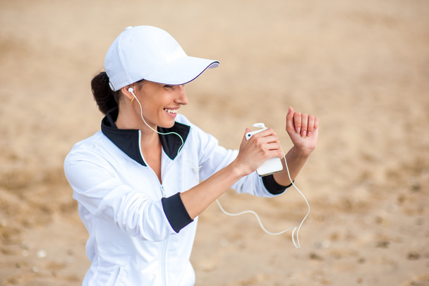 Young woman on beach listening to music in earphones from smart phone mp3 player - Photo, Image