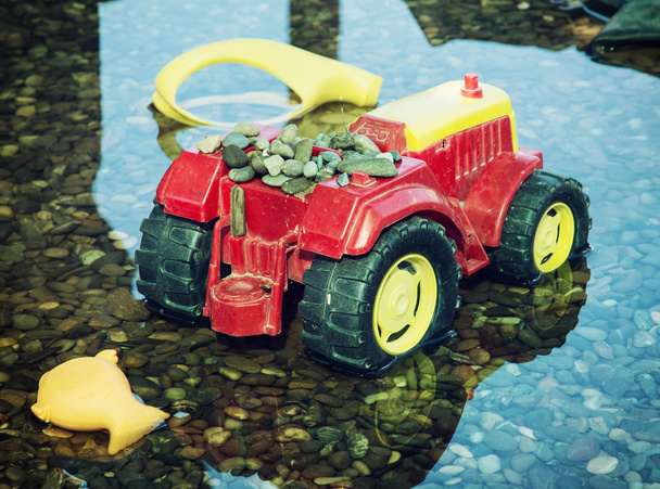 Разноцветный игрушечный трактор отражается в воде
 - Фото, изображение