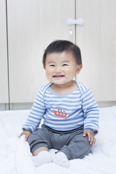Χαριτωμένο μωρό κινεζική αγόρι καθιστός σε ένα λευκό κάλυμμα - Φωτογραφία, εικόνα