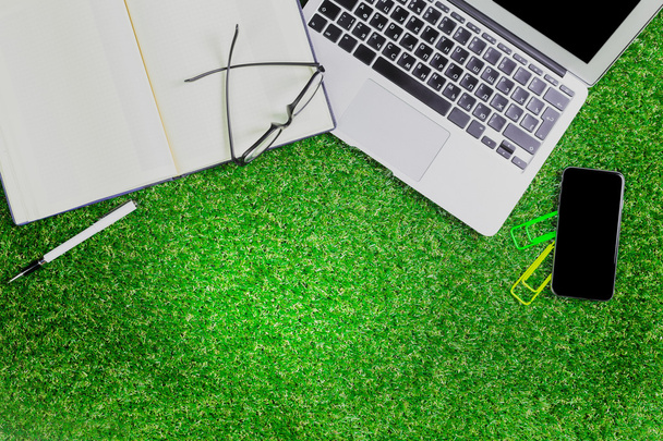 blank notebook, phone, laptop and headphone on green grass - Photo, Image