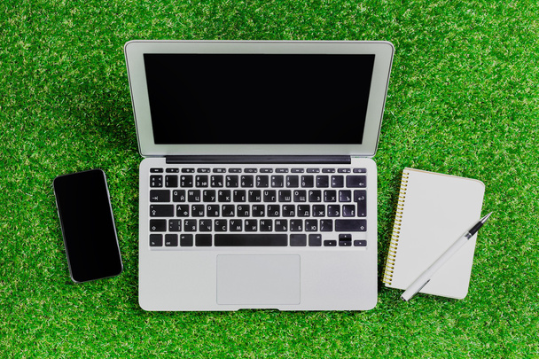 blank notebook, phone, laptop and headphone on green grass - Foto, afbeelding