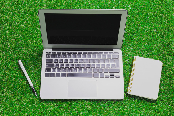 blank notebook, phone, laptop and headphone on green grass - Fotoğraf, Görsel