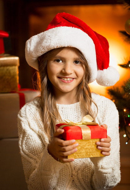 Portrait of cute girl with Christmas gift at fireplace - Fotografie, Obrázek