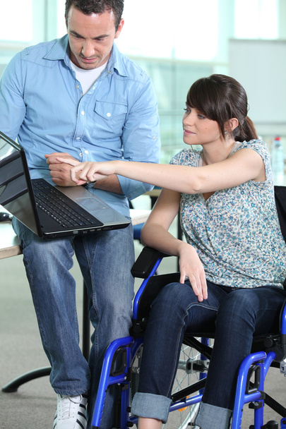 Young woman in wheelchair being shown something on a laptop computer - Foto, afbeelding