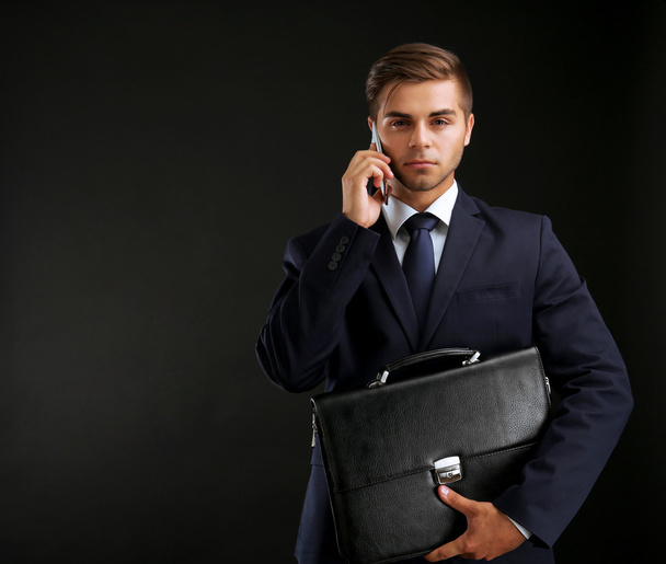 Elegant man in suit with briefcase on dark background - Foto, imagen