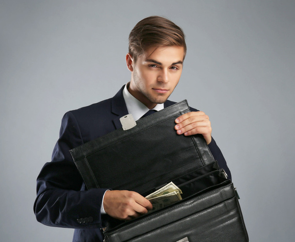 Business man hiding money in briefcase on gray background - Фото, зображення