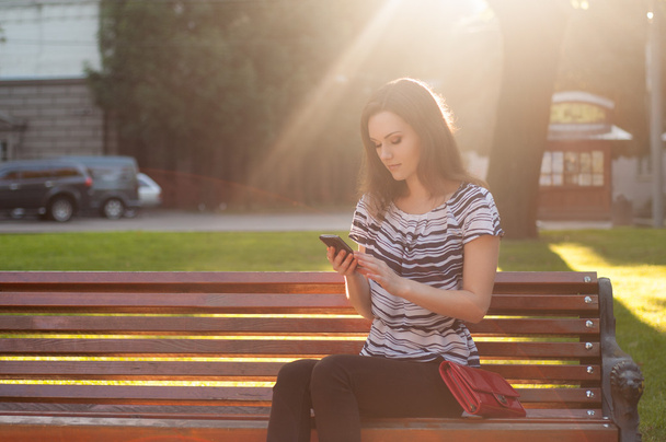 Jeune belle femme assise sur un banc et tapant un message sur
 - Photo, image