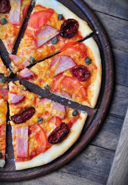 Домашняя пицца с копченым мясом, сушеными и свежими помидорами, каперсами, луком и томатным соусом
 - Фото, изображение