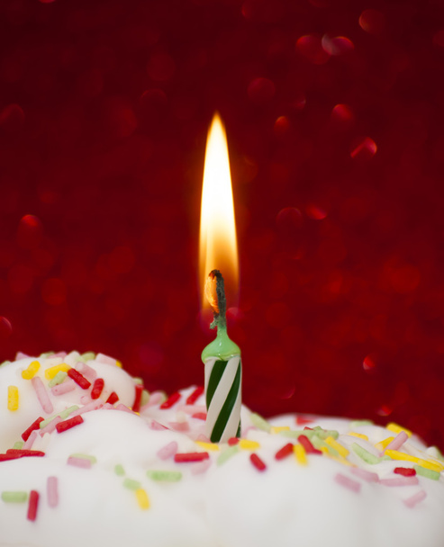 Cupcake with a lit candle over bright red background - Photo, image