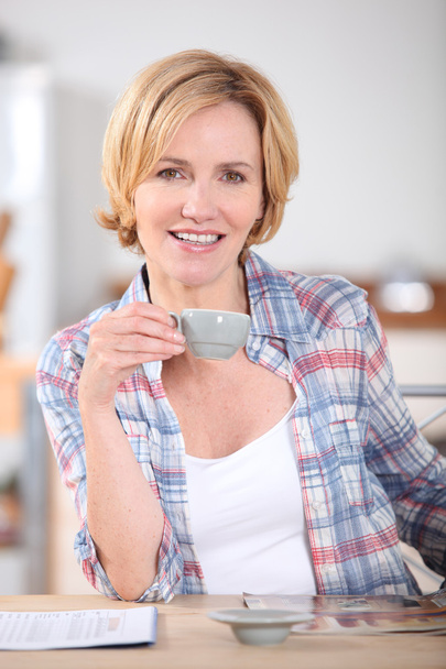 Woman having cup of coffee at kitchen table - Foto, Imagen