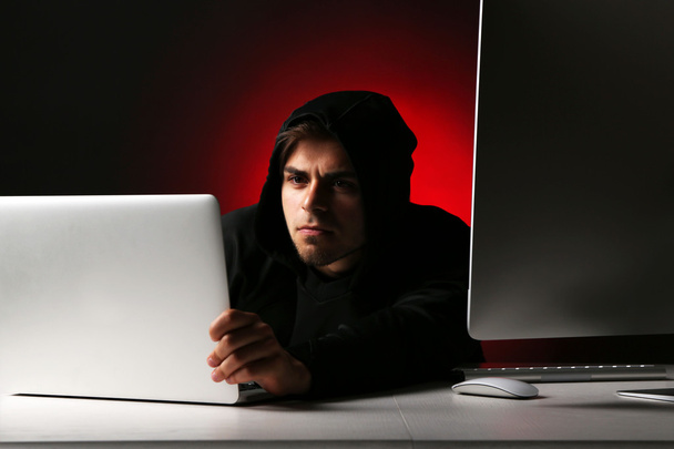 Hacker with computer and laptop on dark background - Photo, image