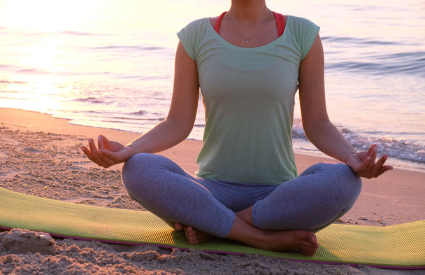 Young healthy woman practicing yoga on the beach at sunset - Photo, Image