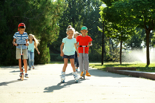 Children riding on scooters and roller skates in park - Foto, Imagen