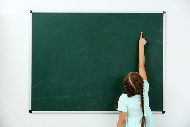 Little girl pointing at something at black chalkboard in classroom - Fotoğraf, Görsel