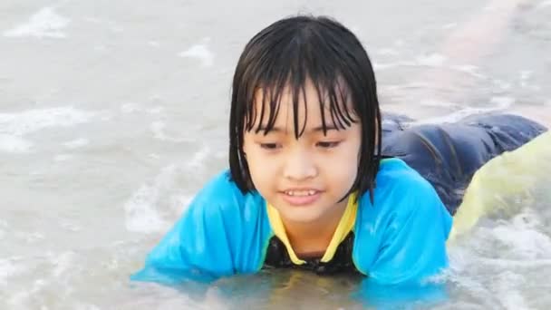 Dziecko azjatyckie zalewaniem w surf na plaży. - Materiał filmowy, wideo