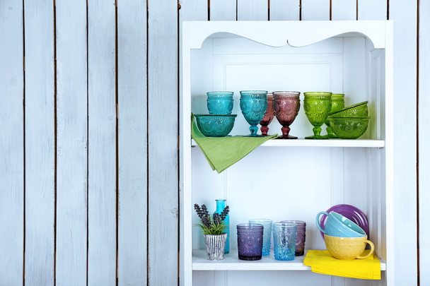 Чистые очки, тарелки и столовые приборы на полках в кухонном шкафу
 - Фото, изображение