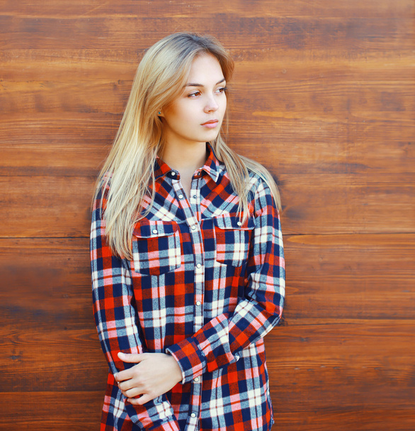 Pretty cool blonde woman in checkered shirt over brown wooden ba - Foto, Imagen