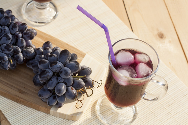 Refrigerador de suco de uva com gelo em vidro e vidro de uvas azuis frescas em uma mesa de madeira close-up, foco seletivo
 - Foto, Imagem