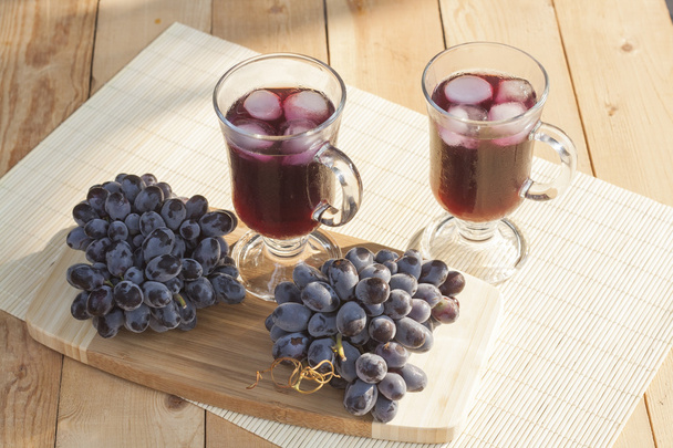Refrigerador de suco de uva com gelo em vidro e vidro de uvas azuis frescas em uma mesa de madeira close-up, foco seletivo
 - Foto, Imagem
