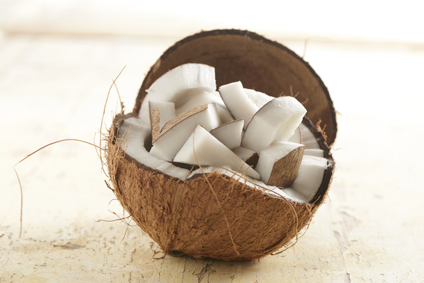 Kokosnuss halb gefüllt mit Kokosstücken auf einem hölzernen Hintergrund - Foto, Bild